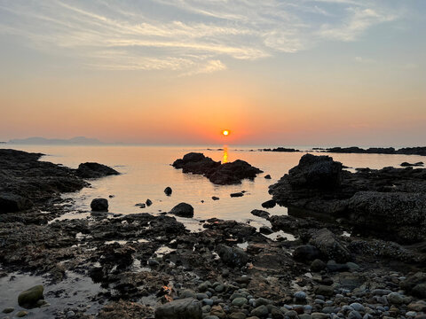 Golden sunset over rocky coastline with calm sea and silhouetted rocks in Taean