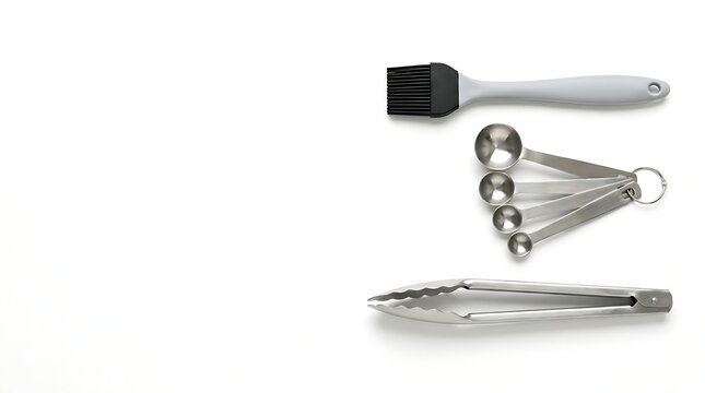 Minimalist composition of stainless steel measuring spoons tongs and silicone basting brush isolated on white background with copy space for culinary and baking concept