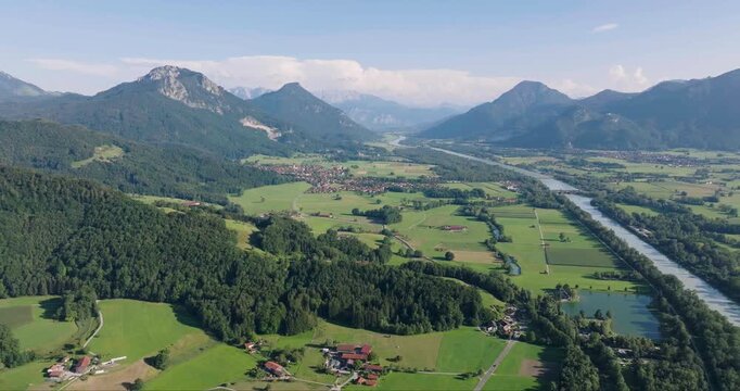 Aerial view of the serene Inn River winding through lush green valleys and dense forests, framed by majestic mountains under a clear sky, Neubeuern, Bavaria, Germany.