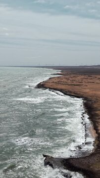 Vertical aerial footage shows dramatic rocky coastline and turquoise waves crashing at Playa Arcoiris, Cabo de la Vela, La Guajira. Bright daylight, wide landscape, vertical video
