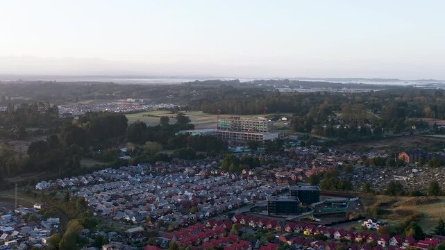 Aerial drone footage at sunrise showing the construction site of the future hospital in Puerto Varas, Chile, with cranes and morning light.
