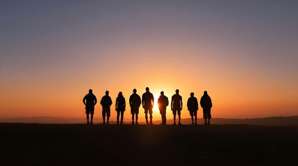 Fototapeta premium A group of people stands together in silhouette against a vibrant golden sunset sky over the open horizon