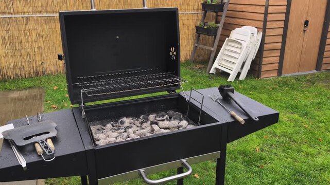 Grilling setup in backyard with charcoal and tools ready for cookout near garden shed