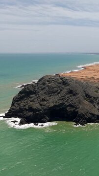 Breathtaking aerial vertical video of Pilon de Azucar at Cabo de la Vela, La Guajira, Colombia. Rugged brown cliffs meet turquoise waves under bright daylight. Ideal for social media.