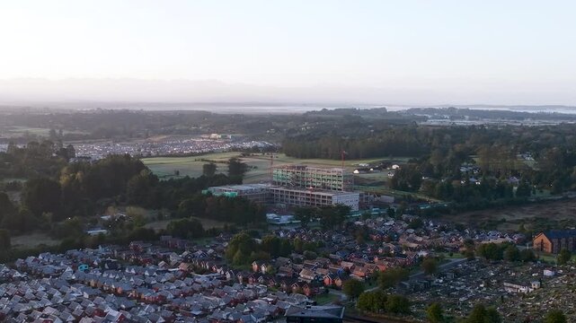 Aerial drone footage at sunrise showing the construction site of the future hospital in Puerto Varas, Chile, with cranes and morning light.