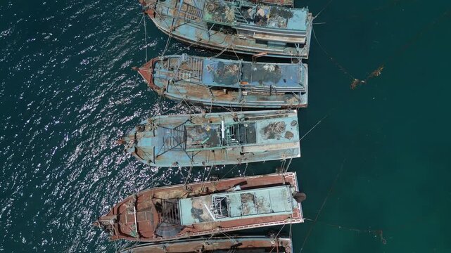 An aerial drone shot featuring a group of decommissioned Indonesian fishing boats tied together in a remote tropical bay. A stark visual of industrial waste and maritime history in Natuna.
