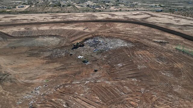 Aerial view of a vast, disturbed brown landscape with a stark white pile of refuse, heavy machinery, and intricate tire tracks, Casa Grande, Arizona, United States.