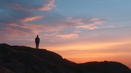 Obraz premium A solitary figure stands atop a mountain ridge against a dramatic and colorful sunset sky