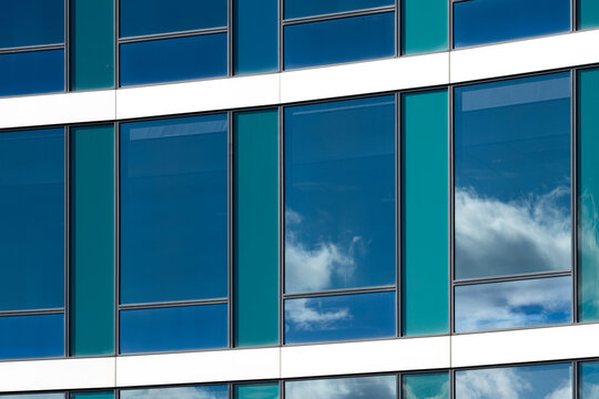 Modern building architecture with glass facade windows and urban skyline as clouds reflection appears in teal geometric grid for contemporary mood