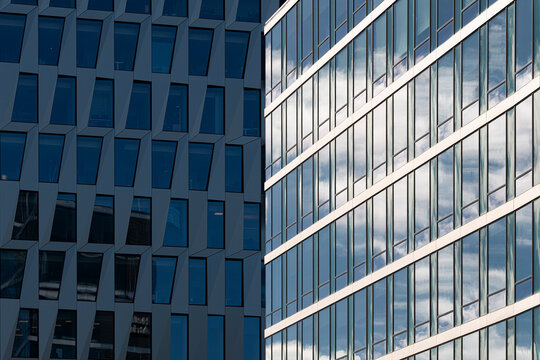 Urban skyline framed by modern building architecture where glass windows and facade overlap with clouds reflection creating diagonal contrast and depth