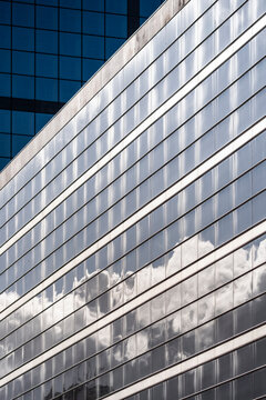Modern building architecture facade with glass windows and urban skyline where clouds reflection runs across crisp horizontal lines and minimal design