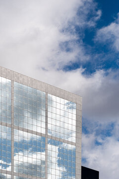 Urban skyline mirrored as clouds reflection across glass windows on modern facade building architecture creating geometric pattern with dynamic angle view