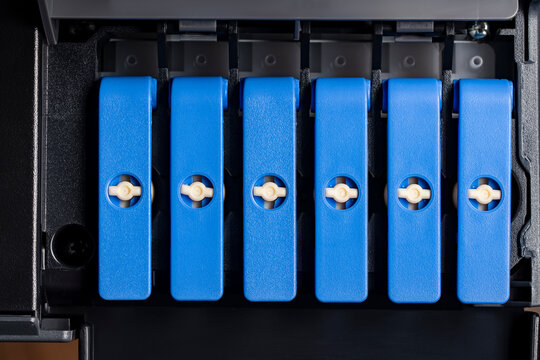 Closeup of blue ink tank caps in photo printer. Macro view of refillable ink tank system caps inside a professional photo printer. Concept of continuous ink supply maintenance and office hardware