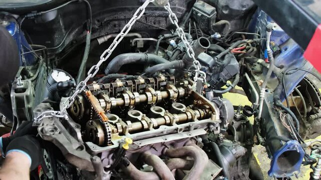 Technician works on fixtures to hold part off floor. Mechanic performs major overhaul on vehicle engine standing in front of under hood compartment