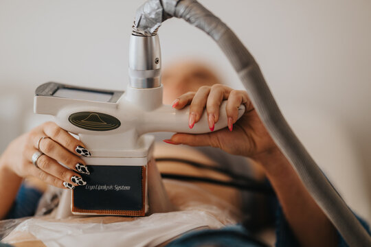 Close-up of a cryolipolysis fat-freezing device held on a woman's abdomen during a cosmetic treatment. A patient receives non-invasive body contouring in a spa setting at a beauty center.