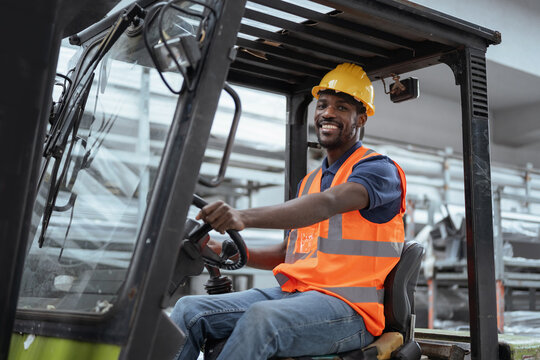 Portrait of a worker operator in a metal warehouse wearing personal protective gear sits in a forklift to transport and load heavy materials.