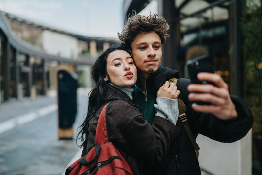Two high school friends pose for a selfie on an urban shopping street. They stand close together while capturing a phone photo of themselves.