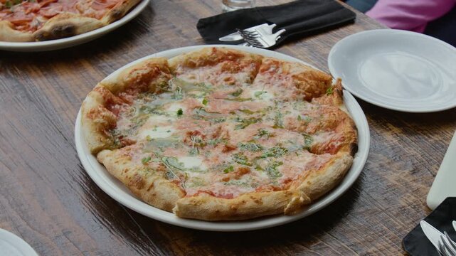Close-up no people view of freshly baked pizza topped with melted mozzarella cheese and pesto sauce on white plate on wooden table in cafe