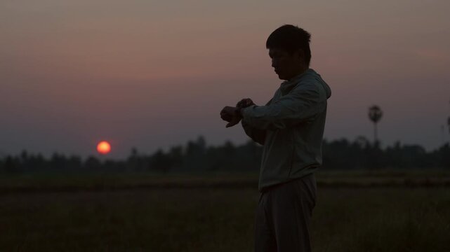 Male runner checking smartwatch during outdoor workout at sunset,