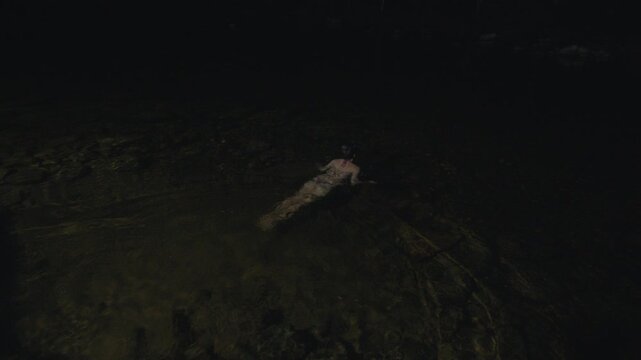 Young woman in bikini enters the river and swims at night