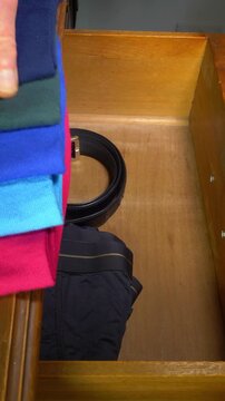 Vertical video social media - Closeup of a senior man&rsquo;s hand neatly placing a belt, then five pairs of different colored folded clean socks, into an open wooden drawer.