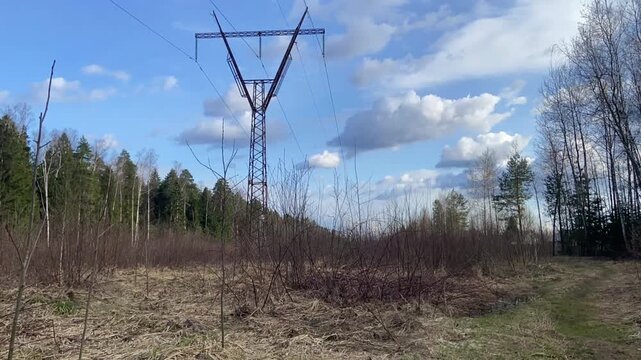 High-voltage electricity transmission tower in a spring forest under blue sky with clouds