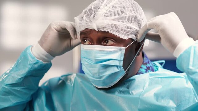 African male surgeon putting on scrub cap and medical face mask, preparing for a medical procedure