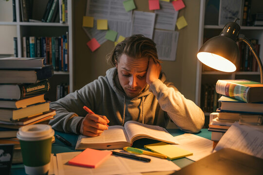 Tired student studying late at night with books and lamp