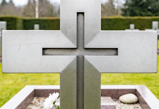 Metal cross headstone with a white flower at the base in a peaceful cemetery, memorial and remembrance for a funeral or tribute in a graveyard setting