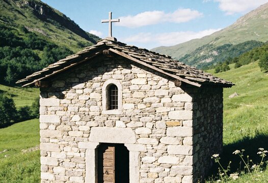 Small stone chapel with a cross standing in a green mountain valley under a blue sky, peaceful religious architecture and historic sanctuary for travel and spiritual retreat