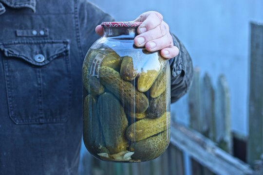 hands holding one big glass jar with green canned cucumbers  in the street