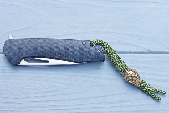 one folding knife with a black handle and a white blade lies on a gray wooden table
