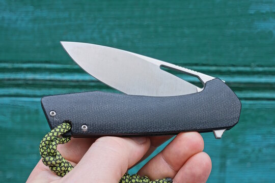 hand holding one folding knife with black handle on green background