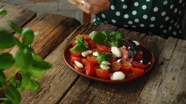 Eating healthy vegetarian salad. Woman adding spices to caprese salad made of chopped tomatoes, mozzarella and basil.