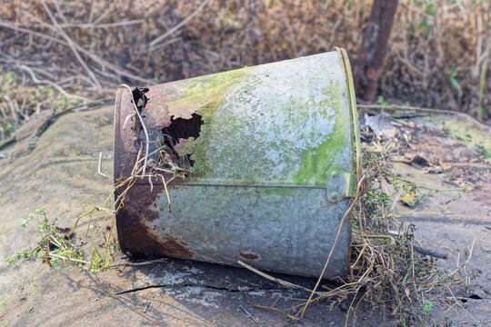 one old broken rusty grey brown bucket with a hole on the ground on the day street