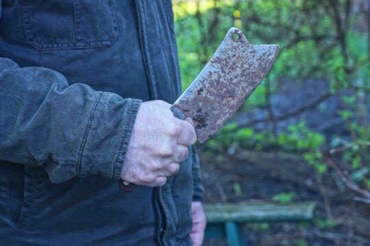 An aggressive man holds an old iron gray cleaver axe in brown rust in one hand on a daytime city street