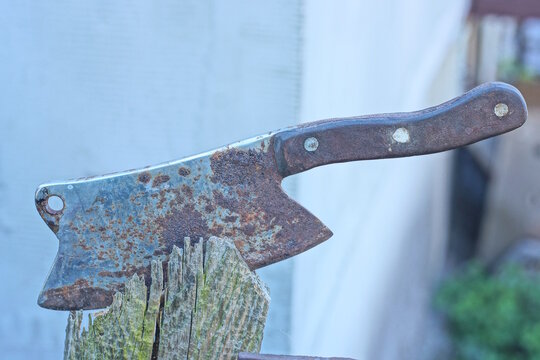 one big old rusty grey brown cleaver axe sticks out in the board of a wooden fence on a daytime street