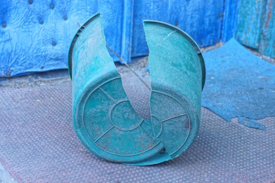 One old broken green plastic bucket stands on the brown floor on the daytime street