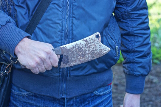 An aggressive man holds an old iron gray cleaver axe in brown rust in one hand on a daytime city street