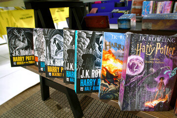 Naklejka premium Minsk, Belarus. Apr 12, 2026. Various Harry Potter books by J.K. Rowling, popular young adult fantasy literature collection showcased on dark wooden furniture stand in bookstore