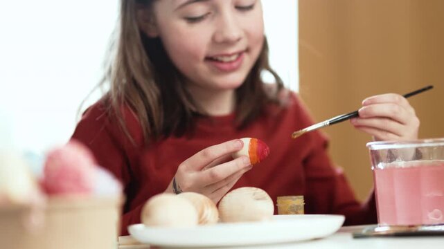 Little girl painting Easter eggs at home, 4K 10-bit cinematic footage of child decorating colorful eggs with watercolor brush for spring holiday, authentic lifestyle.