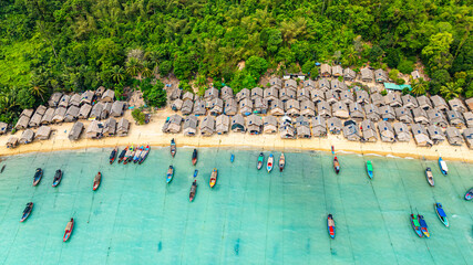 Fototapeta premium Aerial view of Morgan Village hidden in natural beauty on Surin island Phang Nga. small huts along the coastline, surrounded by lush green jungle. fishing boats are anchored in the turquoise waters.