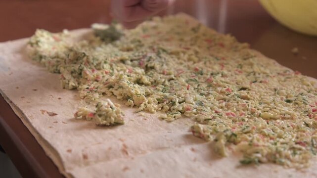 A close-up of a person's hand spreading crab salad filling onto lavash bread
