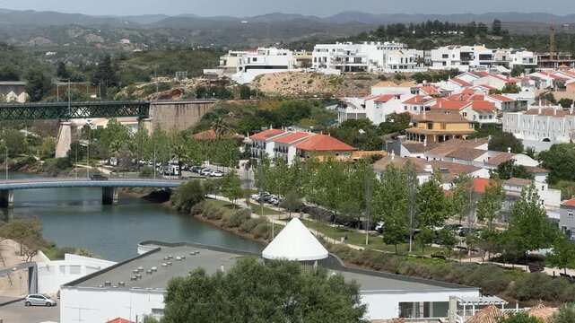 Tavira shows white houses and narrow streets from above, highlighting the tow's layout, greenery, and surrounding hills on a clear day in Algarve, Portugal