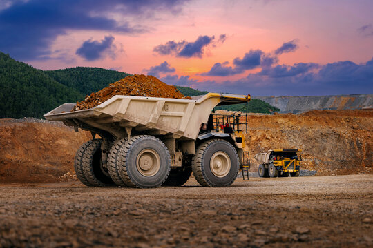 Large loaded haul truck in quarry with gold ore, sunset sky, mining industry concept