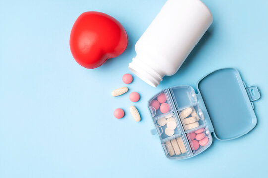 Red heart and various pills, vitamins, dietary supplements on blue background with space for text. Health care, cardiac issues, medical background. Flat lay top view