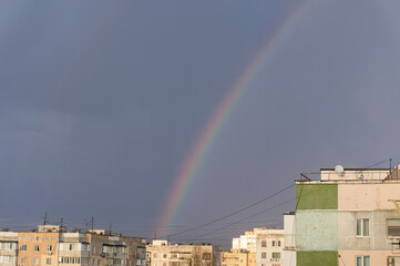Obraz premium Rainbow arch over Soviet-era concrete panel apartment buildings under stormy dramatic sky