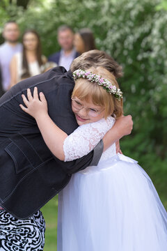 First communion celebration in Poland. Happy blonder girl in white dress, flower wreath and glasses hugging grandmother