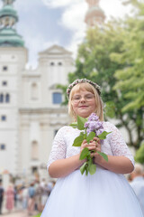 Fototapeta premium First communion celebration in Poland. Happy blonder girl in white dress, flower wreath and glasses