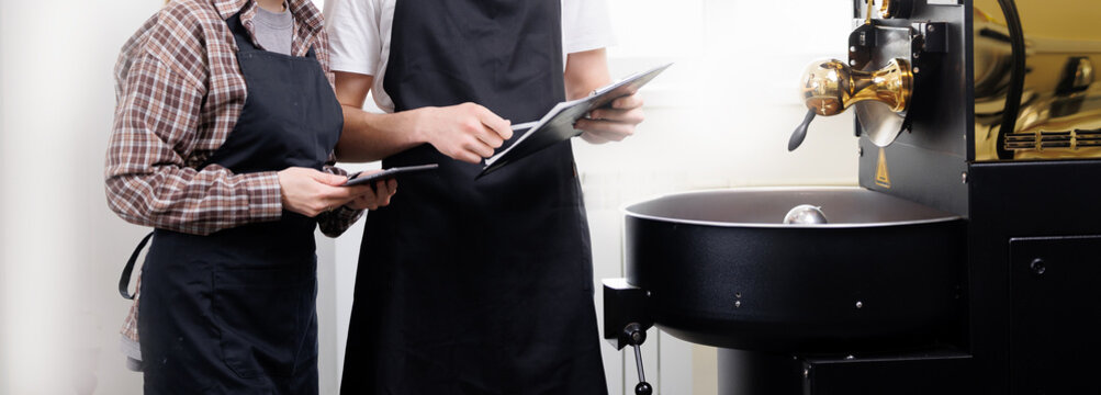 Two workers at coffee factory with roasting equipment and notepads